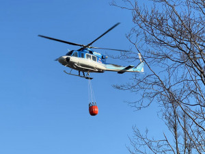 Nad lesním požárem shazuje vodu také posádka vrtulníku