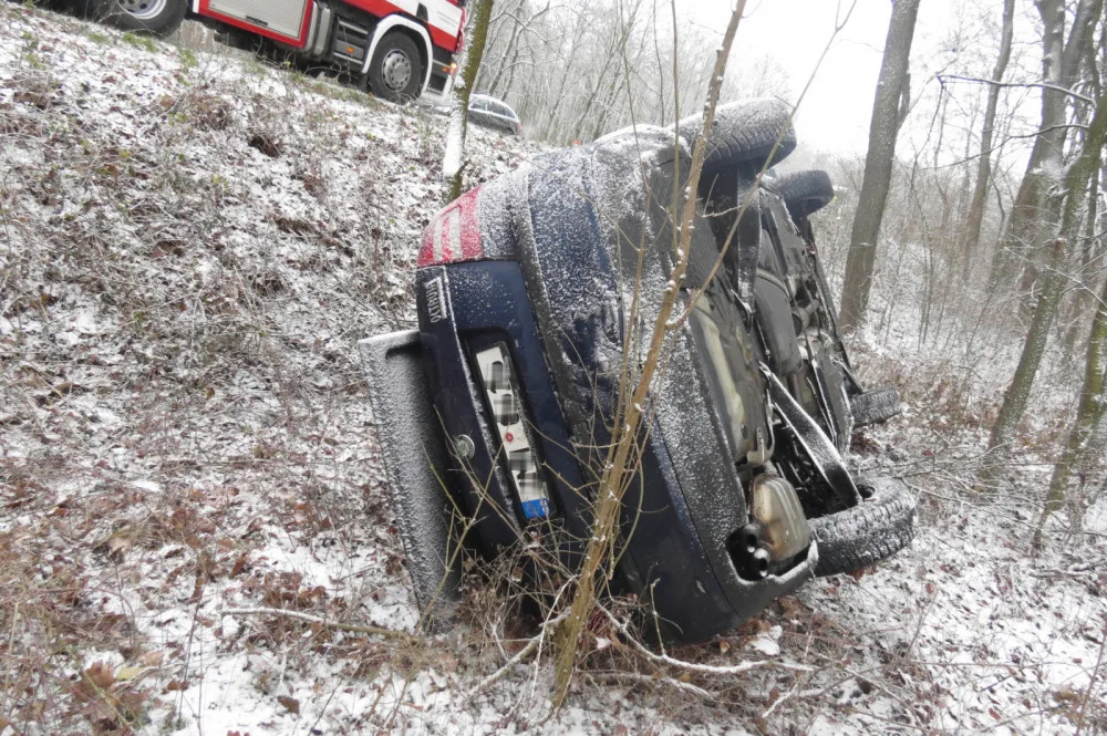 Žena podcenila jízdu po ujetém sněhu a dostala smyk. Škodovka skončila na střeše v blízkém lese